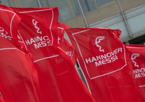 Rote Flaggen mit dem Logo der Hannover Messe vor einer Messehalle