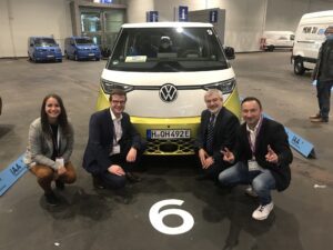 Drei Männer und eine Frau knieend vor einem neuen VW-Bulli