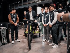 Niedersachsens Wirtschaftsminister Olaf Lies sitzt auf einem Fahrrad mit Wasserstoffantrieb, das ihm Berufsschüler stolz präsentieren.