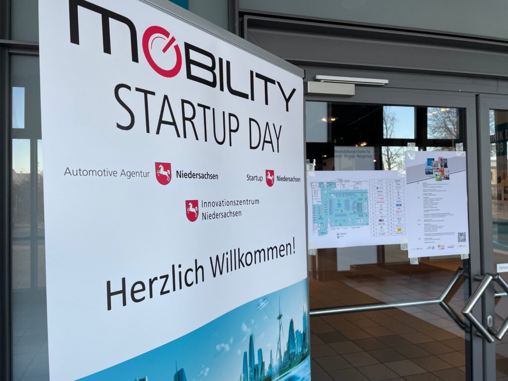 Ein Rollup vor einer Eingangstür mit der Aufschrift Mobility Startup Day - Herzlich willkommen.