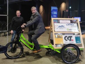 Norbert Gebbe von der Automotive Agentur testet ein wasserstoffangetriebenes Fahrrad mit dreieckigem Werbe-Anhänger