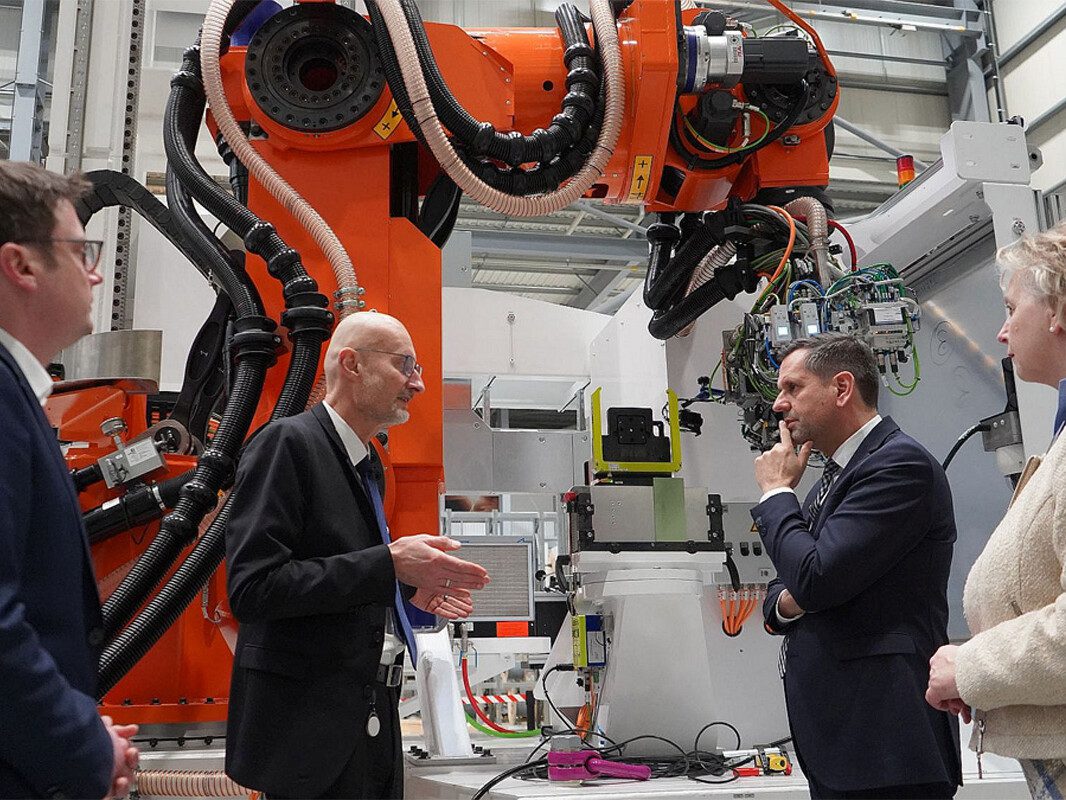 Niedersachsens Wirtschaftsminister Olaf Lies und zwei weitere Besucher bekommen vor einem Roboter etwas erklärt.