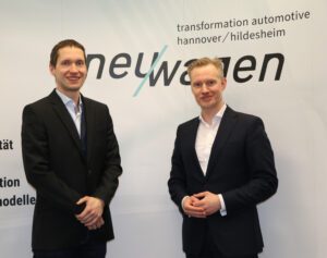 neu/wagen Projektleiter Dr. Michael Merwart und der Fachbereichsleiter Wirtschafts- und Beschäftigungsförderung der Region Hannover, Alexander Skubowius vor einer Plakatwand mit dem Logo des Netzwerks.