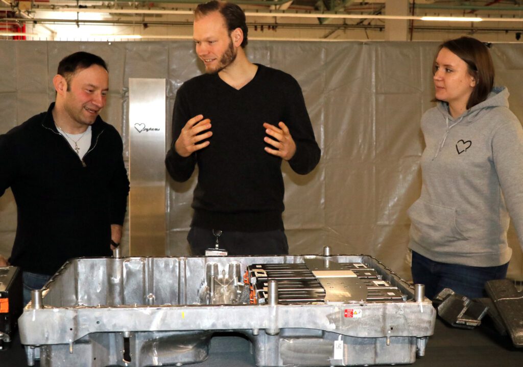 Von links: Olexander Filevych von der Automotive Agentur im Gespräch mit Lasse Bartels und Carina Heidermann von der Firma LB.systems vor einem geöffneten Batteriepack aus einem Hybridauto.