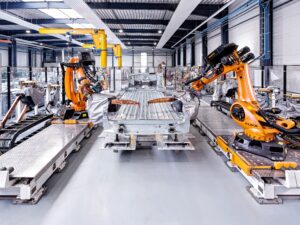 In einer Produktionshalle arbeiten Roboter an einem Fahrzeugunterbau.