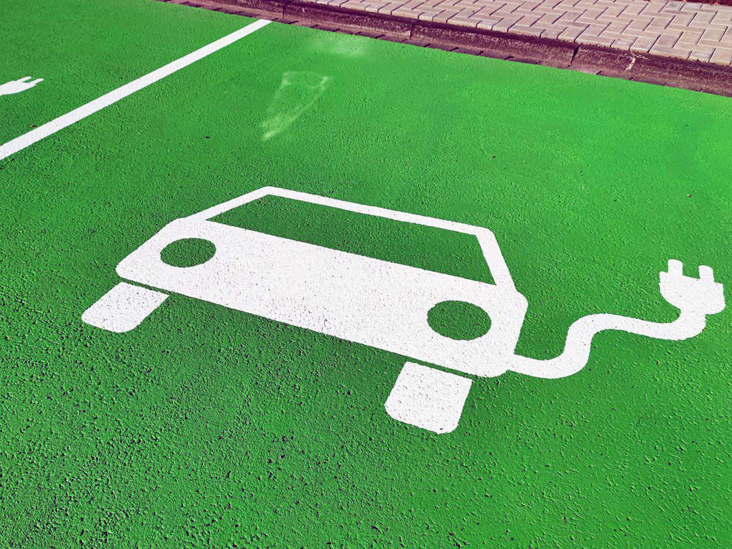 Icon eines Elektroautos auf einem grün gestrichenen Parkplatz.
