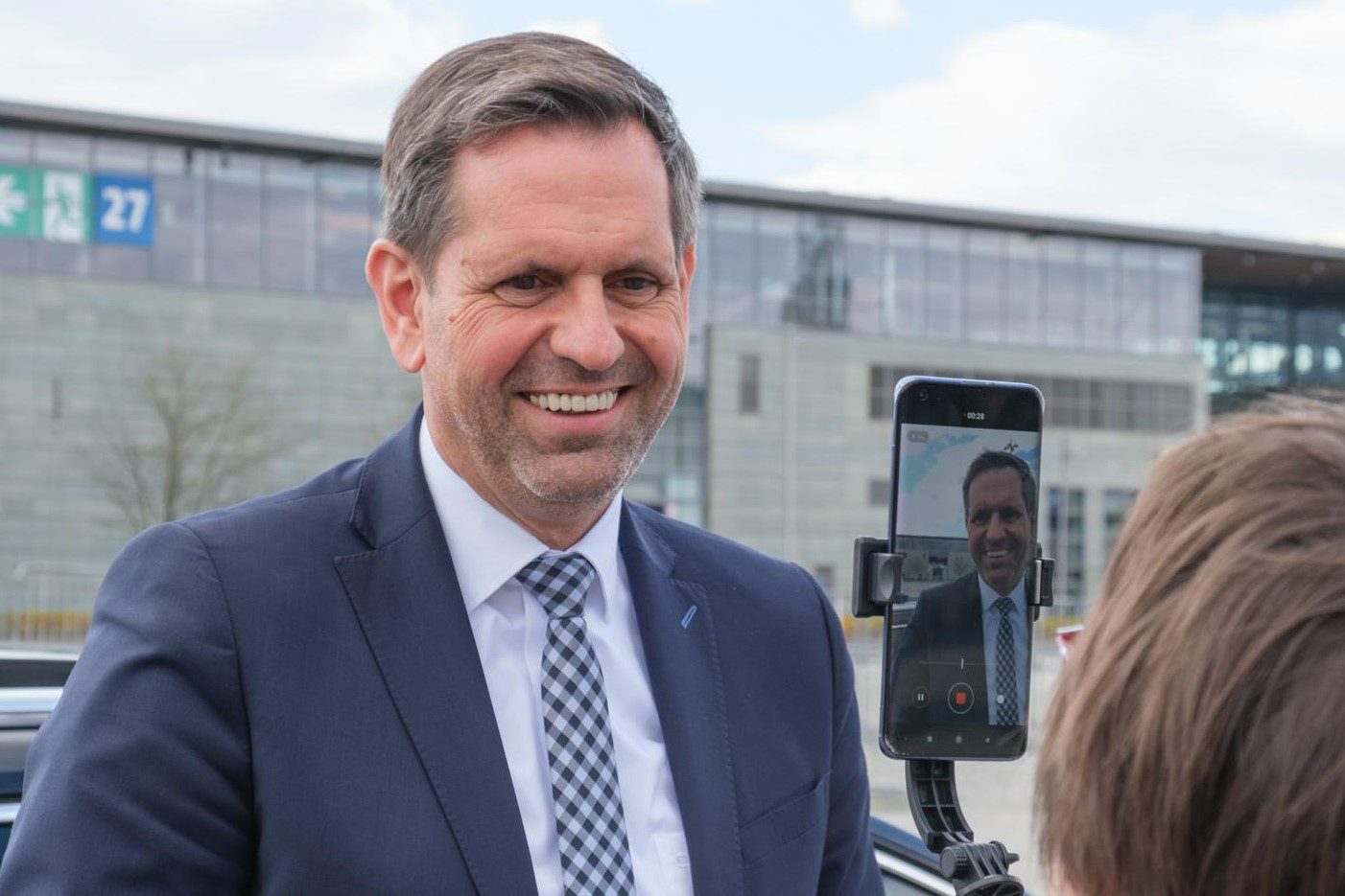 Minister Lies lächelt in eine Handykamera